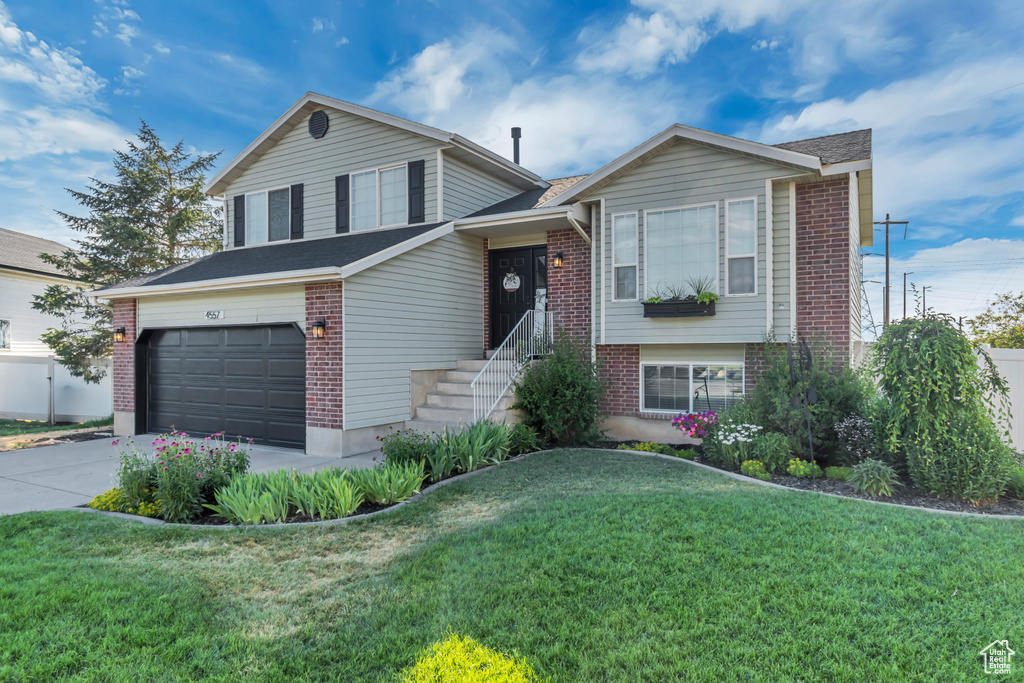 Tri-level home with brick siding, driveway, a front yard, and a shingled roof