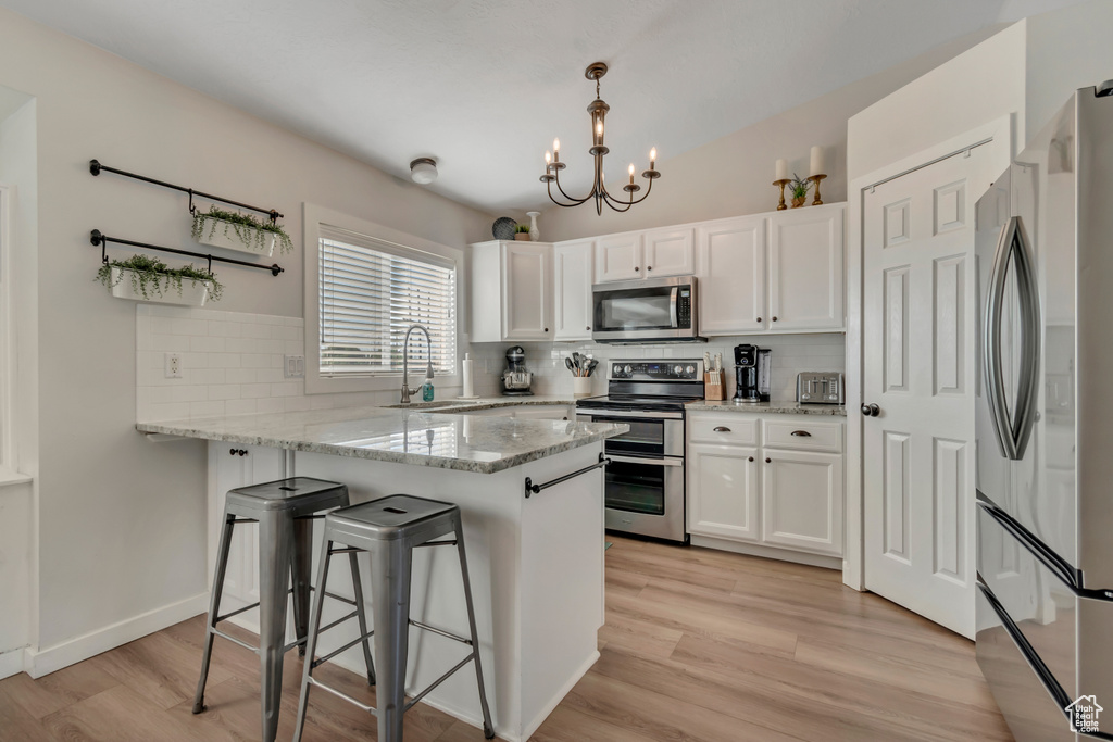 Kitchen featuring stainless steel appliances, a peninsula, white cabinetry, a chandelier, and tasteful backsplash