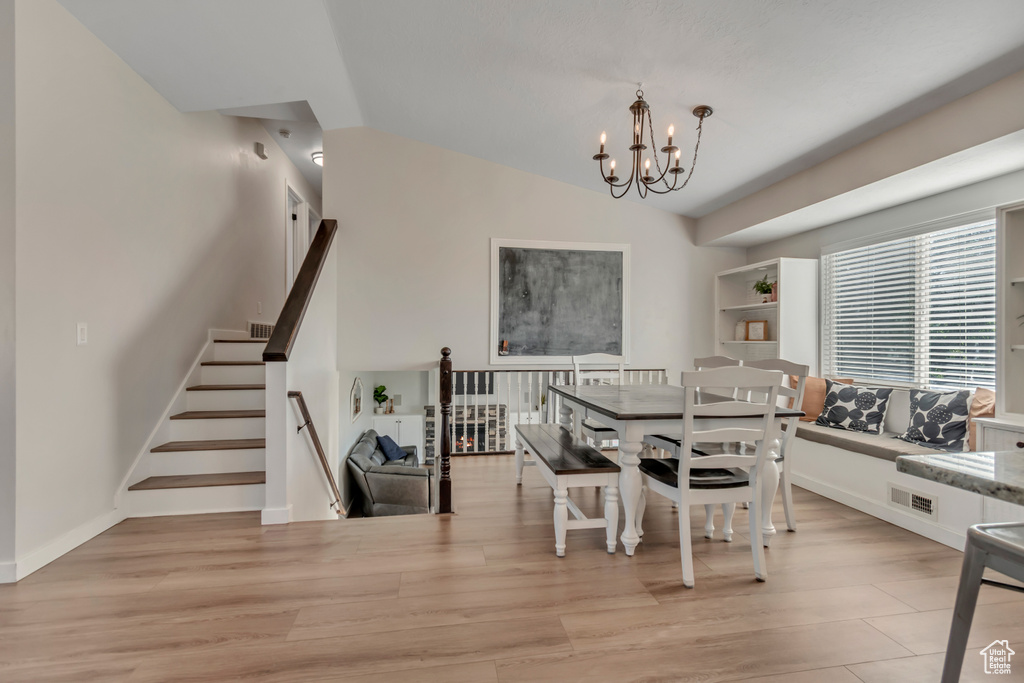 Dining space with a chandelier, light wood-style flooring, stairs, and lofted ceiling