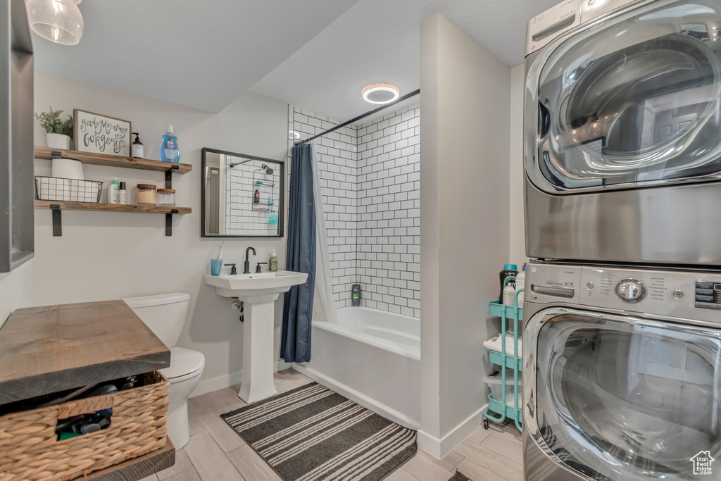 Full bath with stacked washer / drying machine, shower / tub combo with curtain, and wood tiled floors