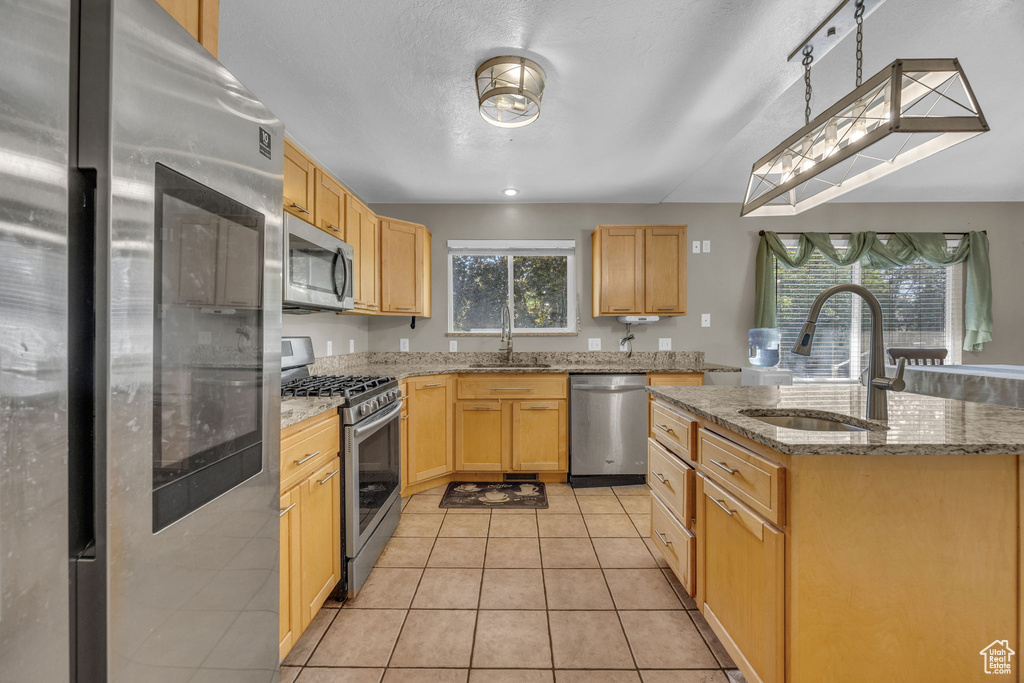 Kitchen with appliances with stainless steel finishes, light brown cabinetry, an island with sink, light tile patterned floors, and light stone countertops