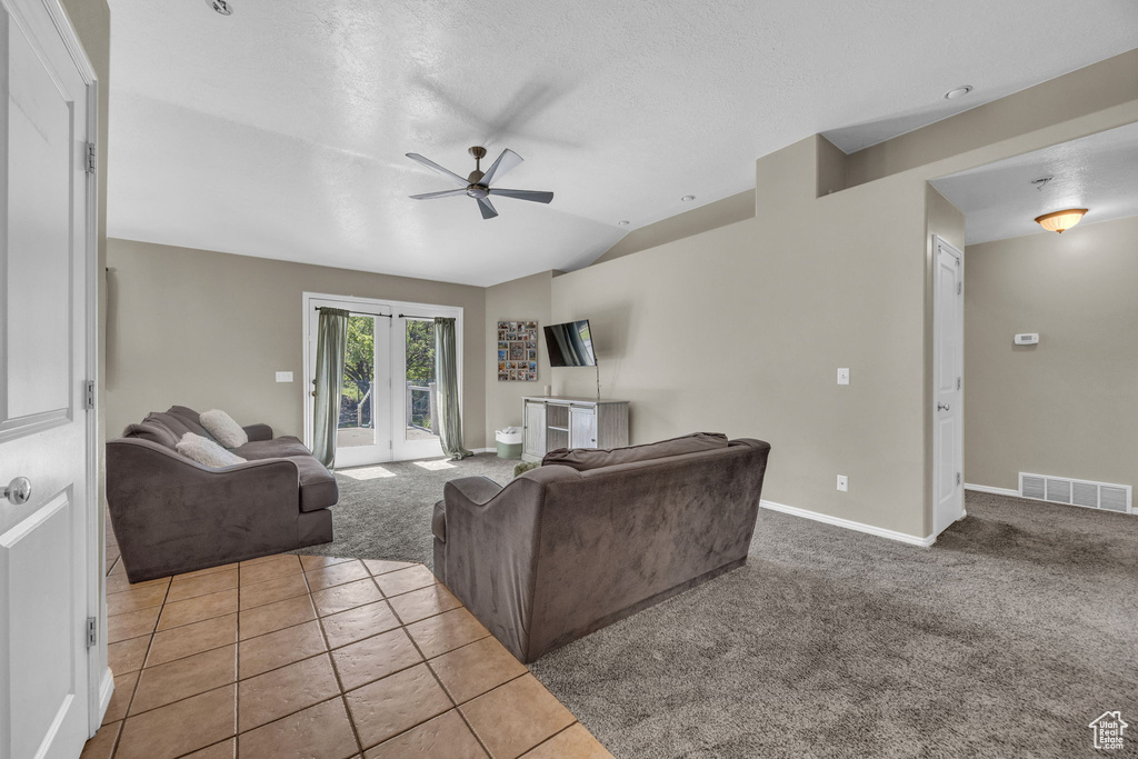 Carpeted living area featuring ceiling fan, lofted ceiling, french doors, and tile patterned floors