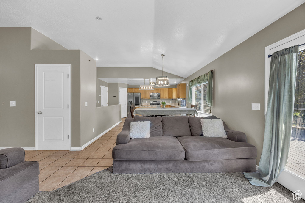 Living room featuring vaulted ceiling, light tile patterned floors, healthy amount of natural light, and a chandelier