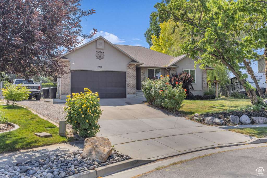 View of front of home featuring brick siding, driveway, a garage, a front lawn, and stucco siding