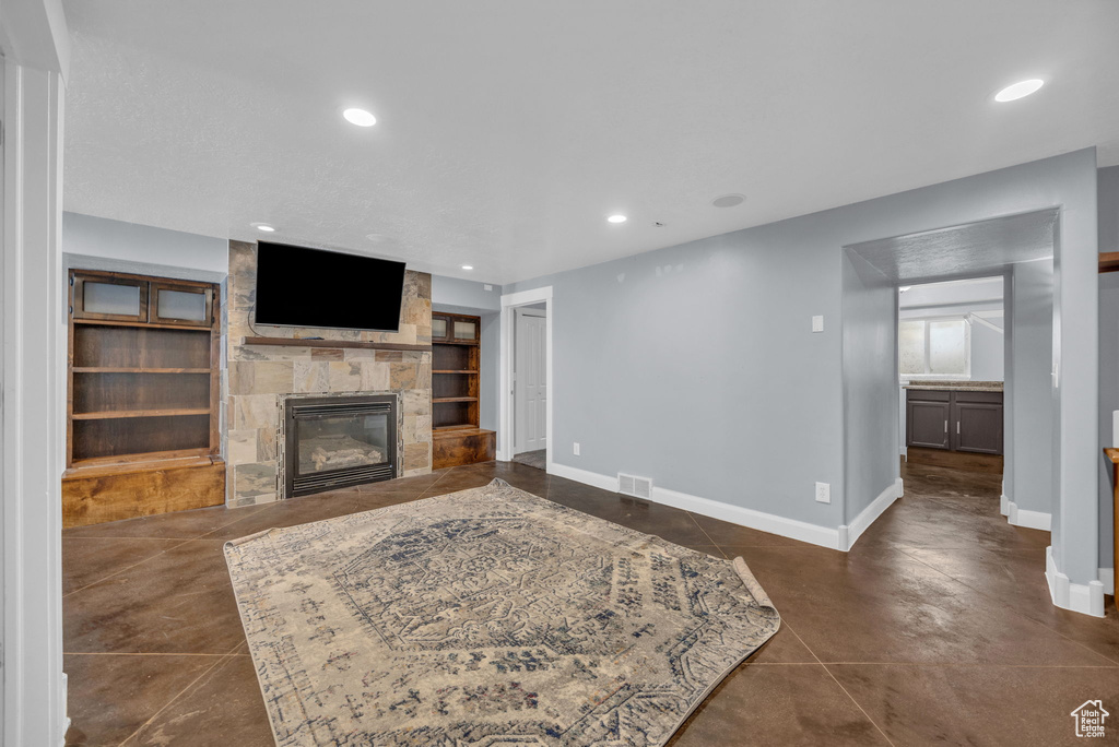 Living area with a stone fireplace, built in shelves, recessed lighting, and concrete floors