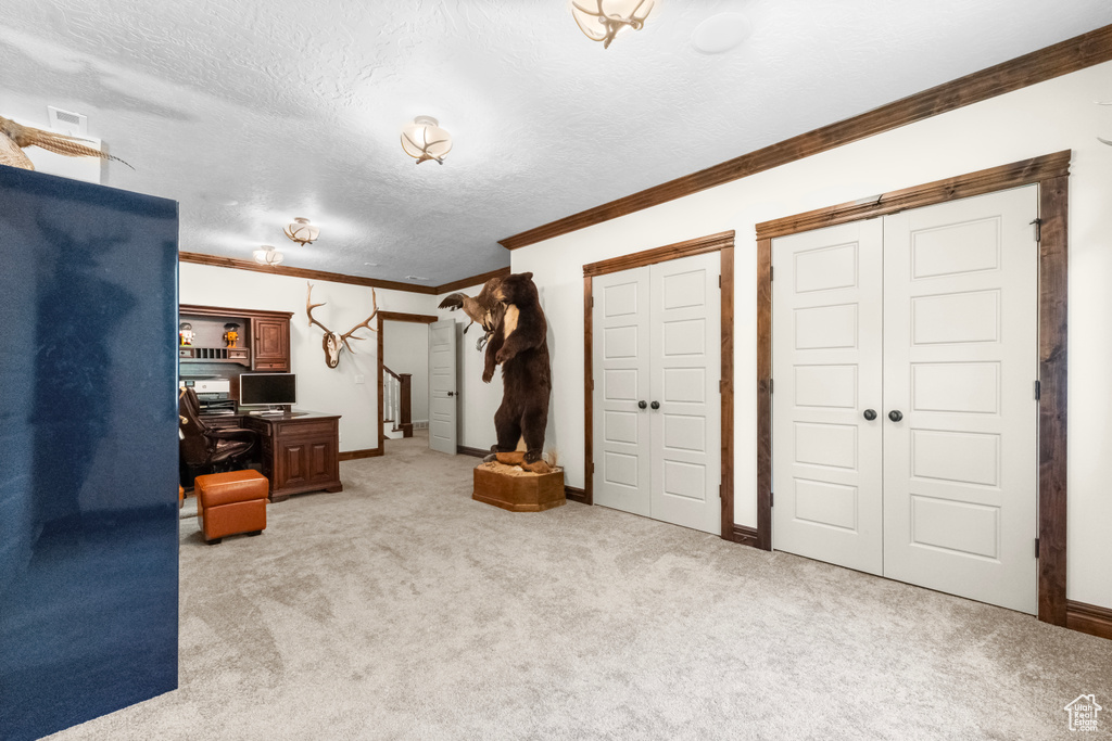 Unfurnished bedroom with crown molding, a desk, light colored carpet, and a textured ceiling