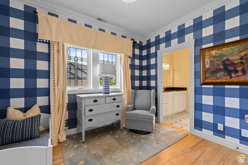 Sitting room with wallpapered walls, light wood-style flooring, and crown molding