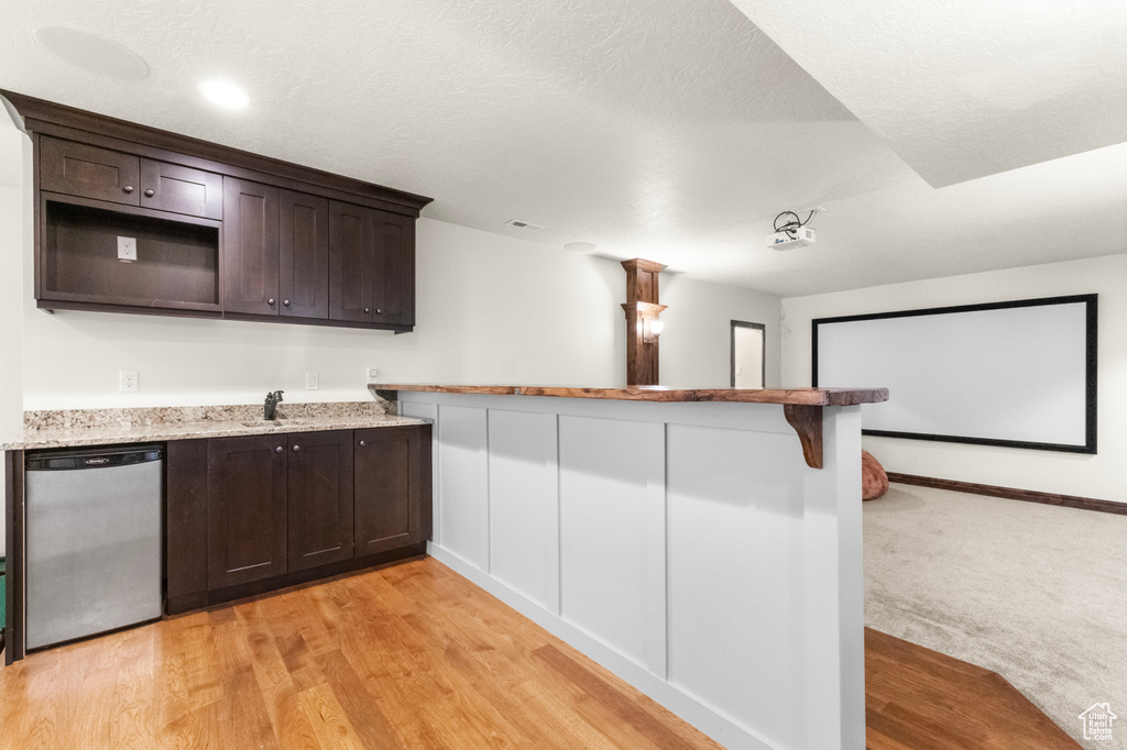 Kitchen featuring stainless steel dishwasher, dark brown cabinetry, a peninsula, and light stone counters