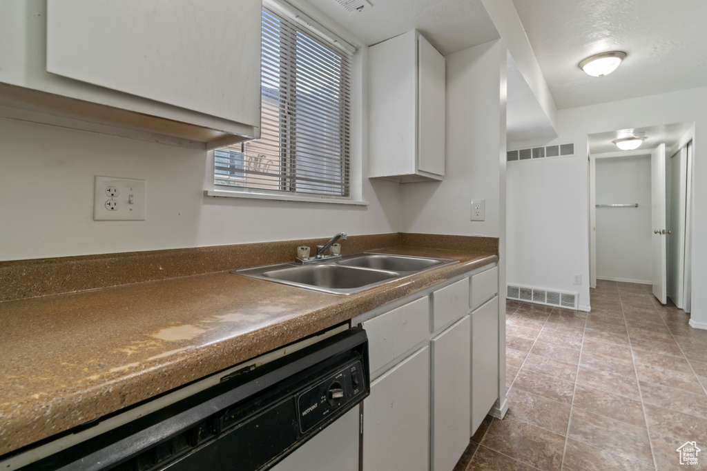 Kitchen featuring white dishwasher, white cabinets, and dark countertops