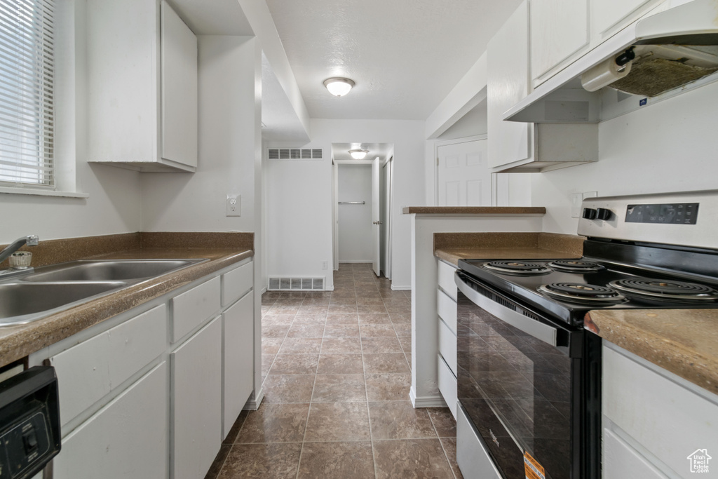 Kitchen with electric range, under cabinet range hood, white cabinets, and dark countertops
