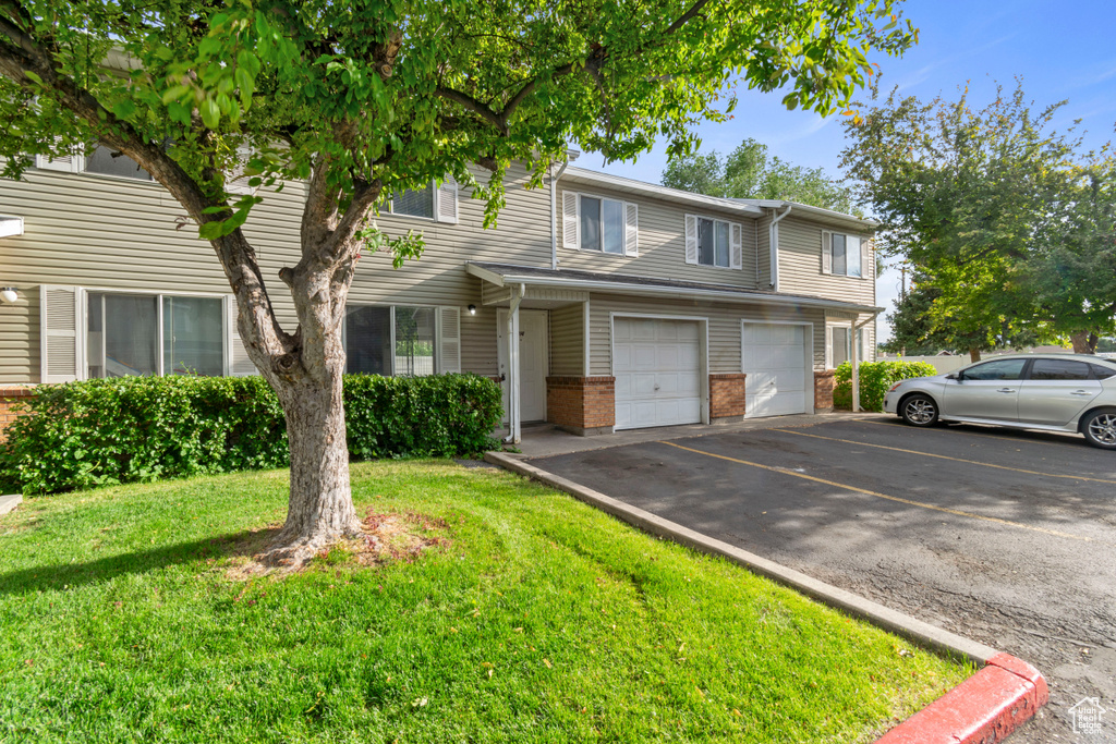 Townhome / multi-family property featuring asphalt driveway, a garage, brick siding, and a front yard