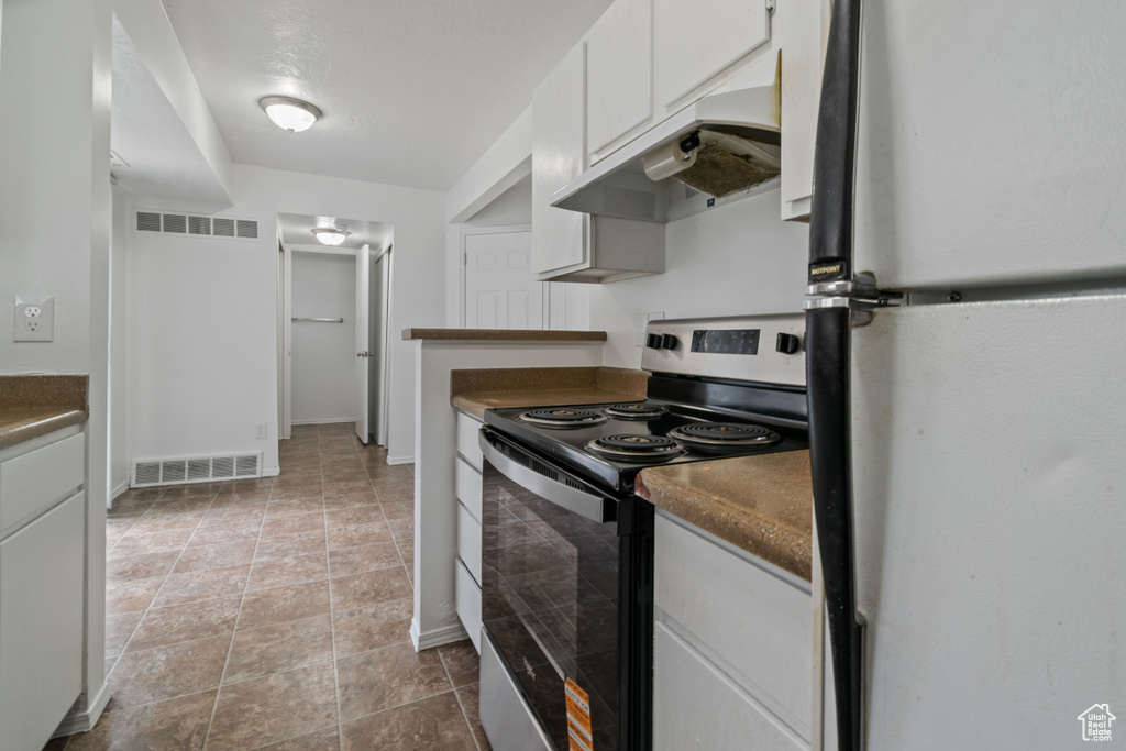 Kitchen with freestanding refrigerator, stainless steel electric range, under cabinet range hood, dark countertops, and white cabinetry