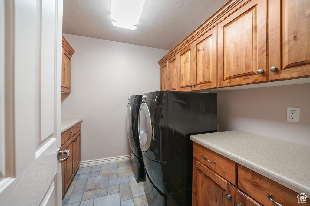 Laundry area with cabinet space, washer and dryer, and light stone finish floors