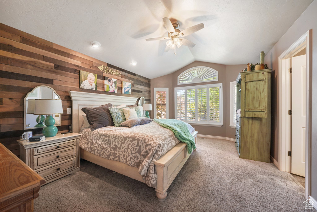 Carpeted bedroom with lofted ceiling, wood walls, and ceiling fan