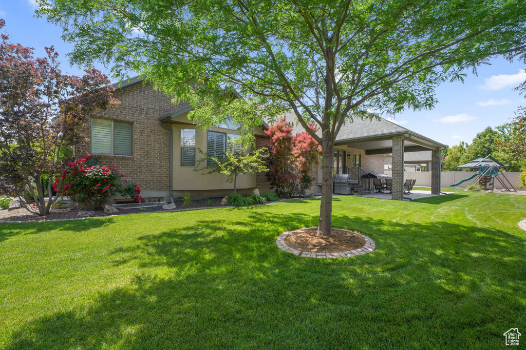 Back of house with a playground, a patio area, and brick siding