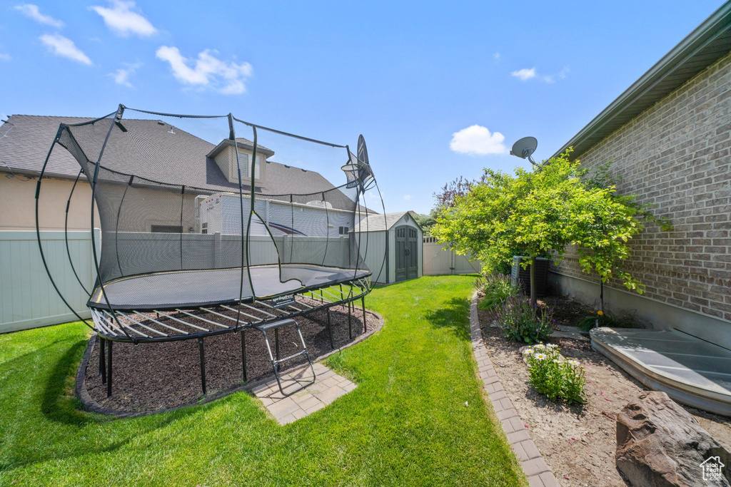 Fenced backyard featuring a trampoline and a storage unit
