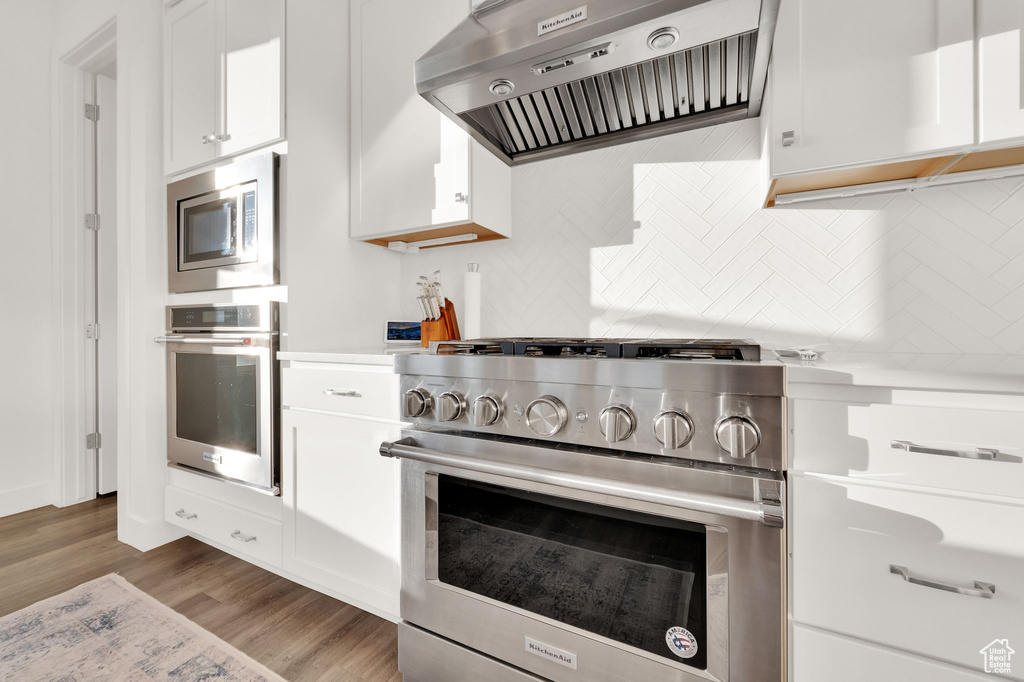 Kitchen featuring range hood, appliances with stainless steel finishes, wood finished floors, white cabinetry, and light countertops