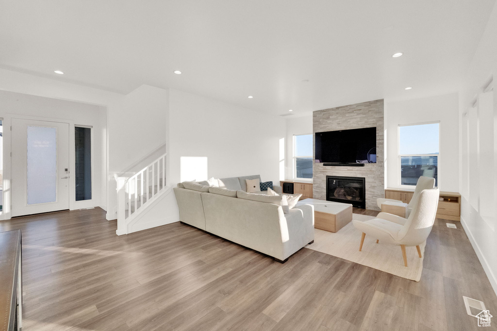 Living area with light wood finished floors, a stone fireplace, recessed lighting, and stairway