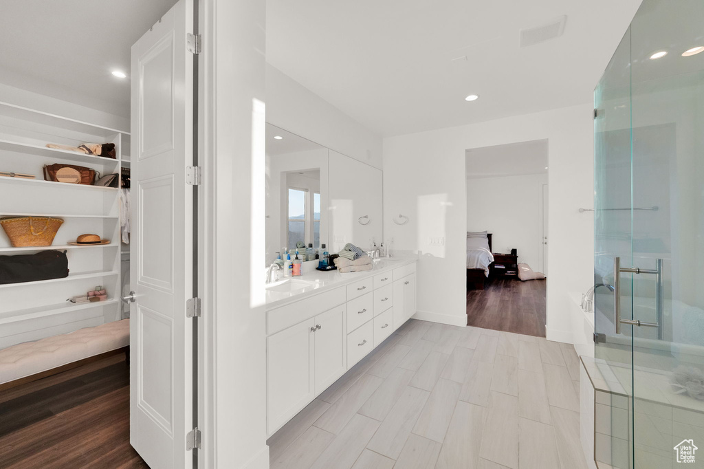 Ensuite bathroom with double vanity, a stall shower, recessed lighting, wood finished floors, and a closet