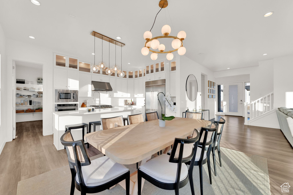 Dining space with light wood-type flooring, a chandelier, recessed lighting, and stairs