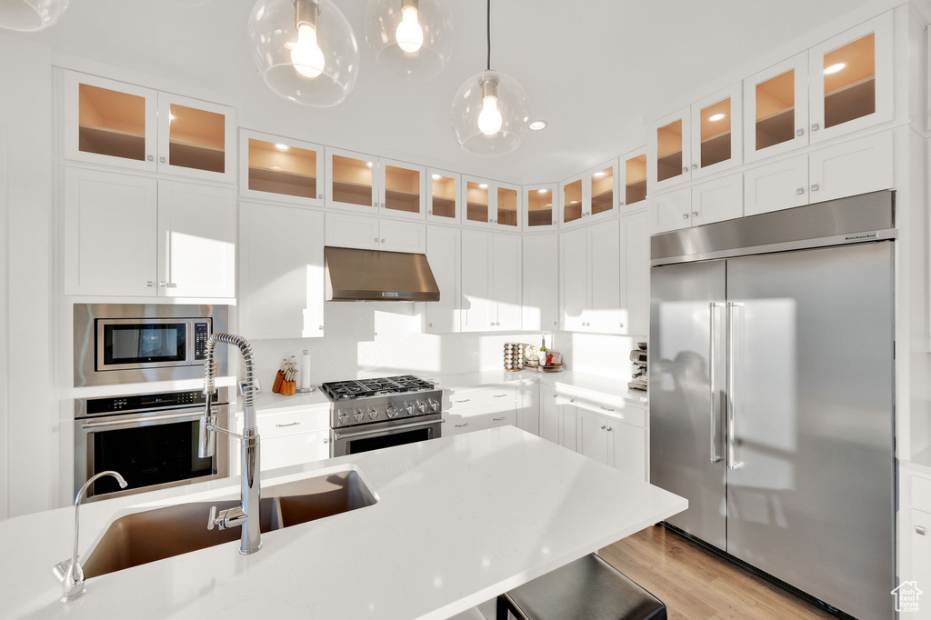 Kitchen featuring built in appliances, under cabinet range hood, light countertops, decorative light fixtures, and light wood-style flooring