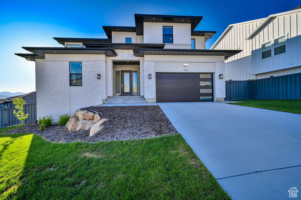 View of front facade featuring driveway, stone siding, and a garage