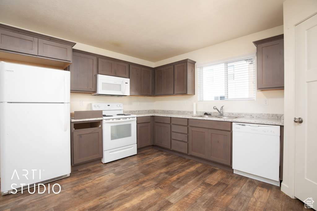 Kitchen with white appliances, dark brown cabinetry, and dark wood-style flooring