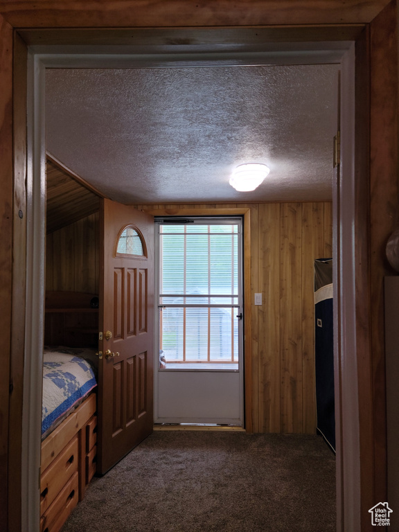 Unfurnished bedroom featuring a textured ceiling, dark colored carpet, and wooden walls