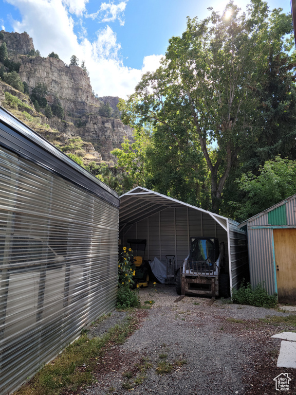 View of parking with a carport, gravel driveway, a mountain view, and a storage shed