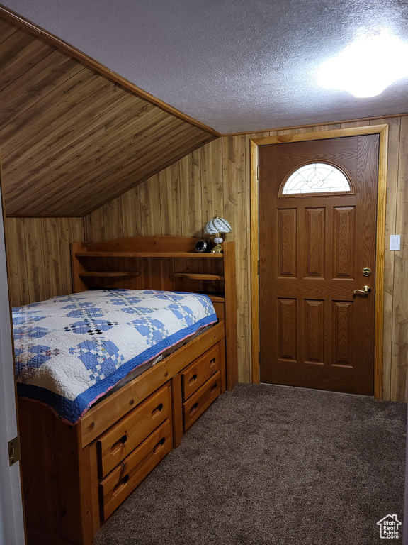 Bedroom featuring wood walls, vaulted ceiling, carpet, and a textured ceiling