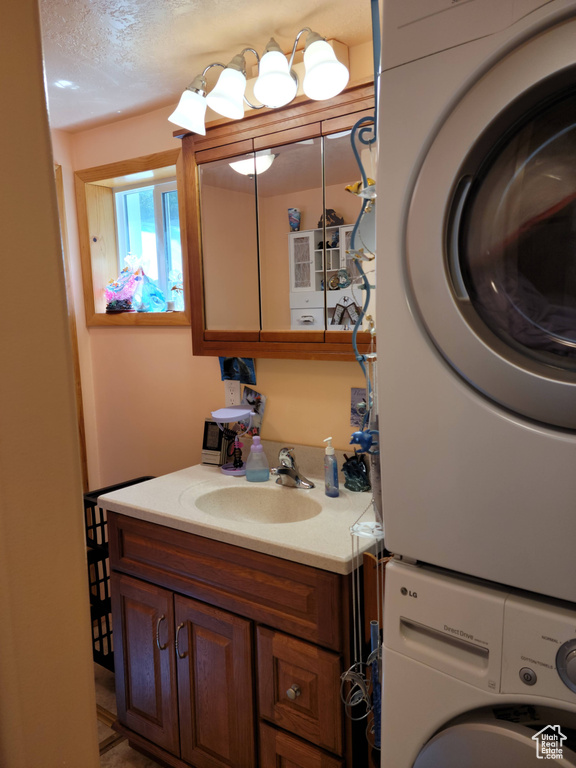 Bathroom with stacked washer / drying machine, vanity, and a textured ceiling