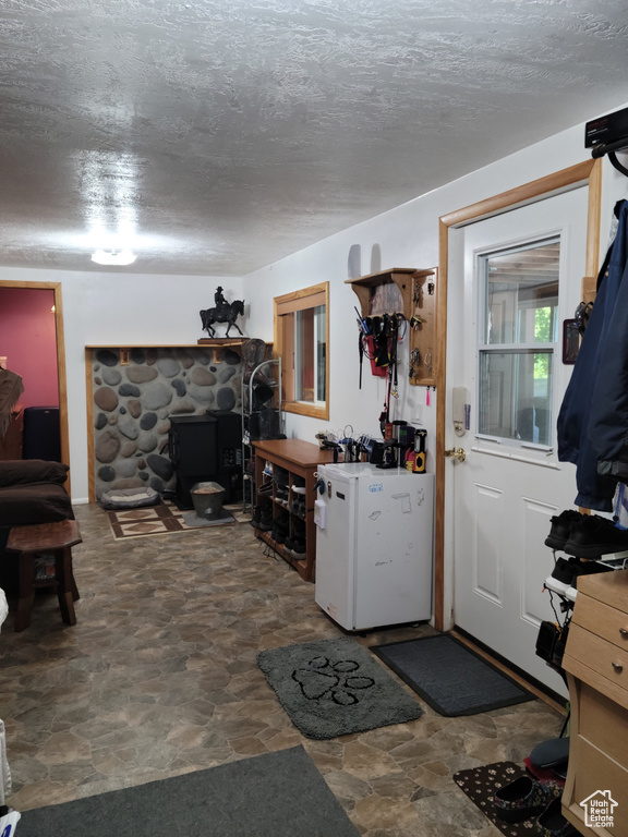 Kitchen with stone finish flooring, fridge, a textured ceiling, and a wood stove