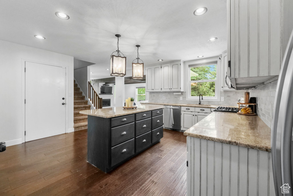 Kitchen featuring dishwasher, a center island, dark wood finished floors, tasteful backsplash, and pendant lighting