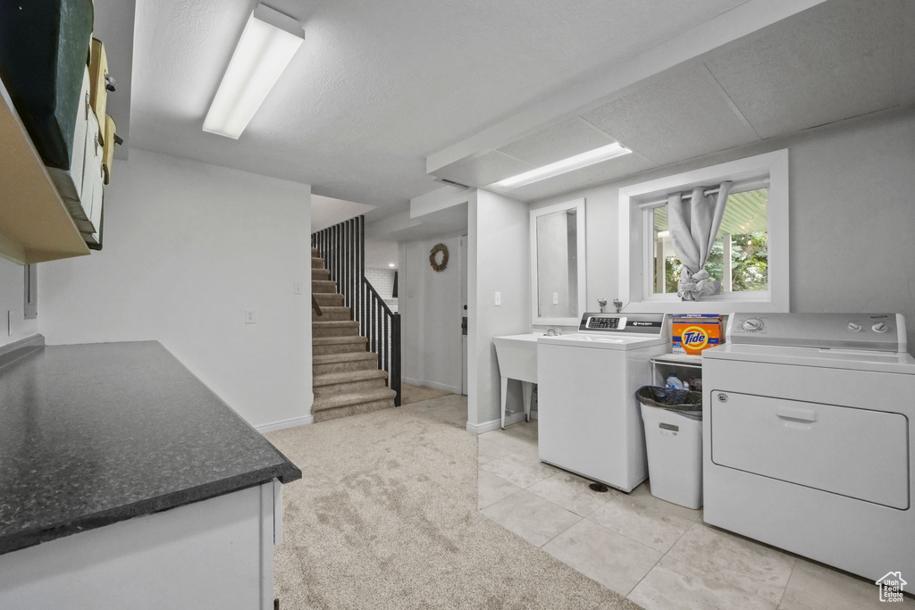 Kitchen featuring washer and dryer, light tile patterned floors, and white cabinetry