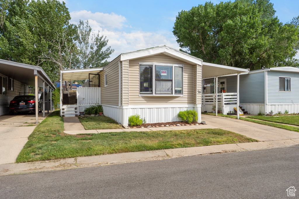 Manufactured / mobile home featuring driveway, an attached carport, a front yard, and covered porch