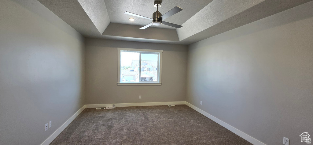 Empty room with a tray ceiling, a textured ceiling, ceiling fan, and dark carpet