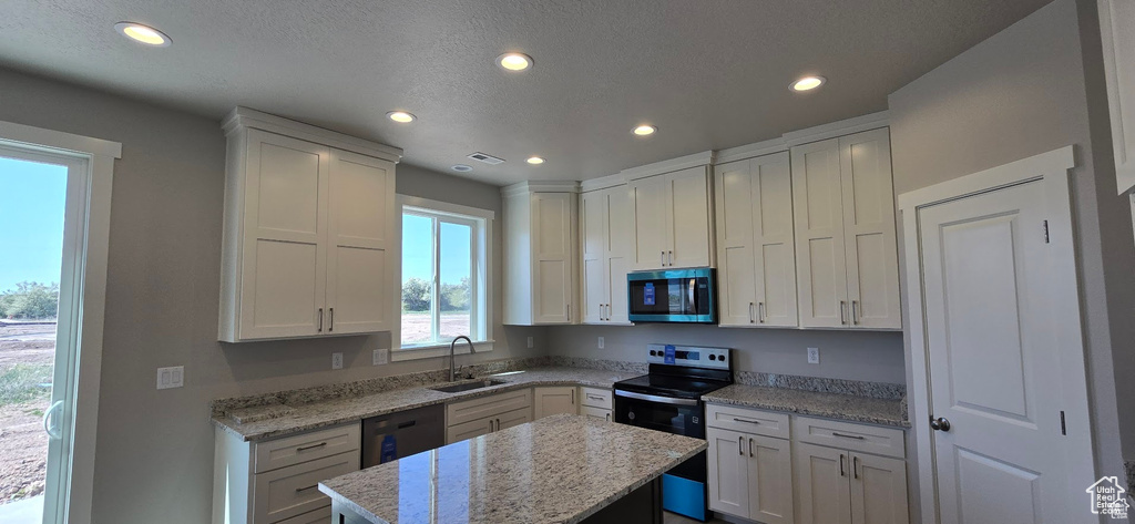 Kitchen with appliances with stainless steel finishes, recessed lighting, white cabinetry, a kitchen island, and light stone counters