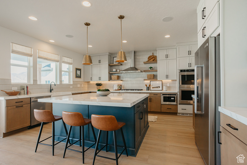 Kitchen with appliances with stainless steel finishes, tasteful backsplash, open shelves, light stone counters, and a kitchen breakfast bar