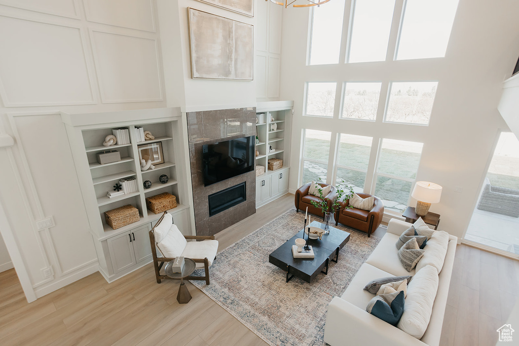 Living area featuring a tile fireplace, light wood-type flooring, plenty of natural light, and a high ceiling