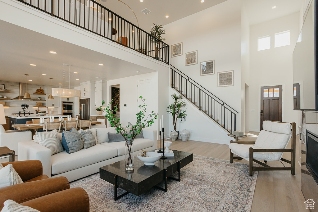 Living area featuring light wood-style floors, a towering ceiling, healthy amount of natural light, stairway, and recessed lighting