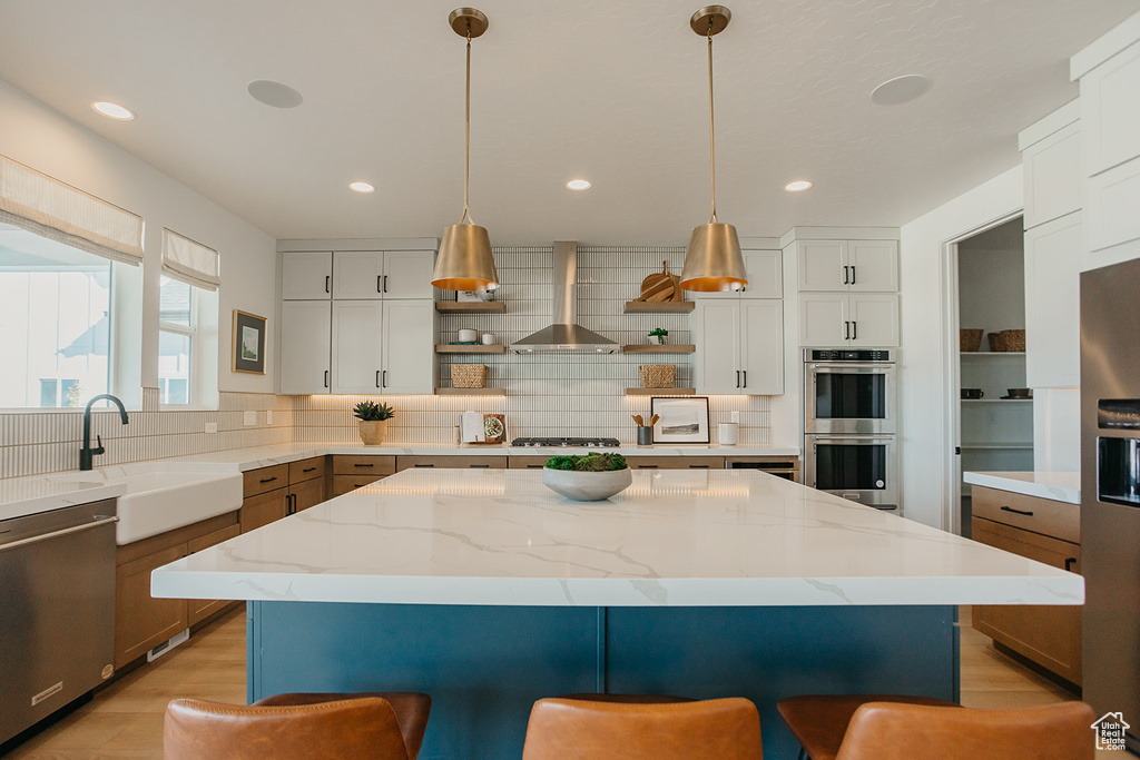 Kitchen featuring wall chimney range hood, appliances with stainless steel finishes, open shelves, a breakfast bar area, and decorative backsplash