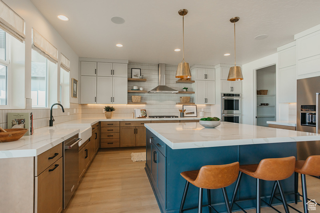 Kitchen with open shelves, stainless steel appliances, wall chimney exhaust hood, a kitchen breakfast bar, and tasteful backsplash