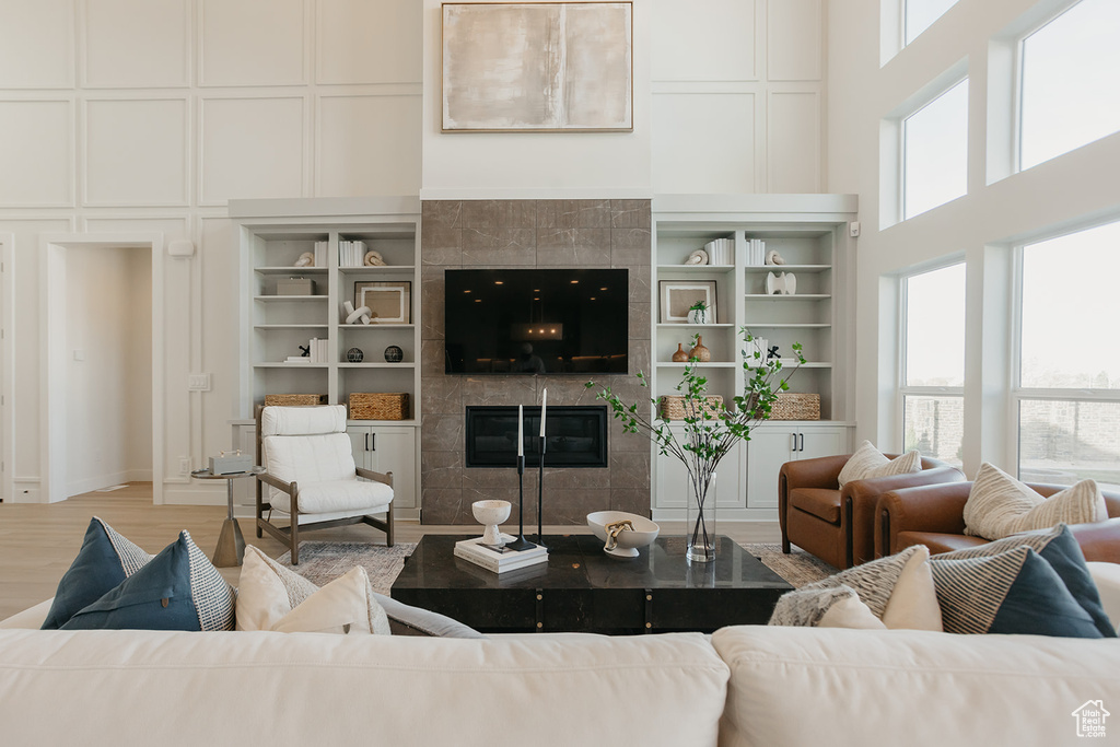 Living area with a tiled fireplace, a decorative wall, a high ceiling, and wood finished floors