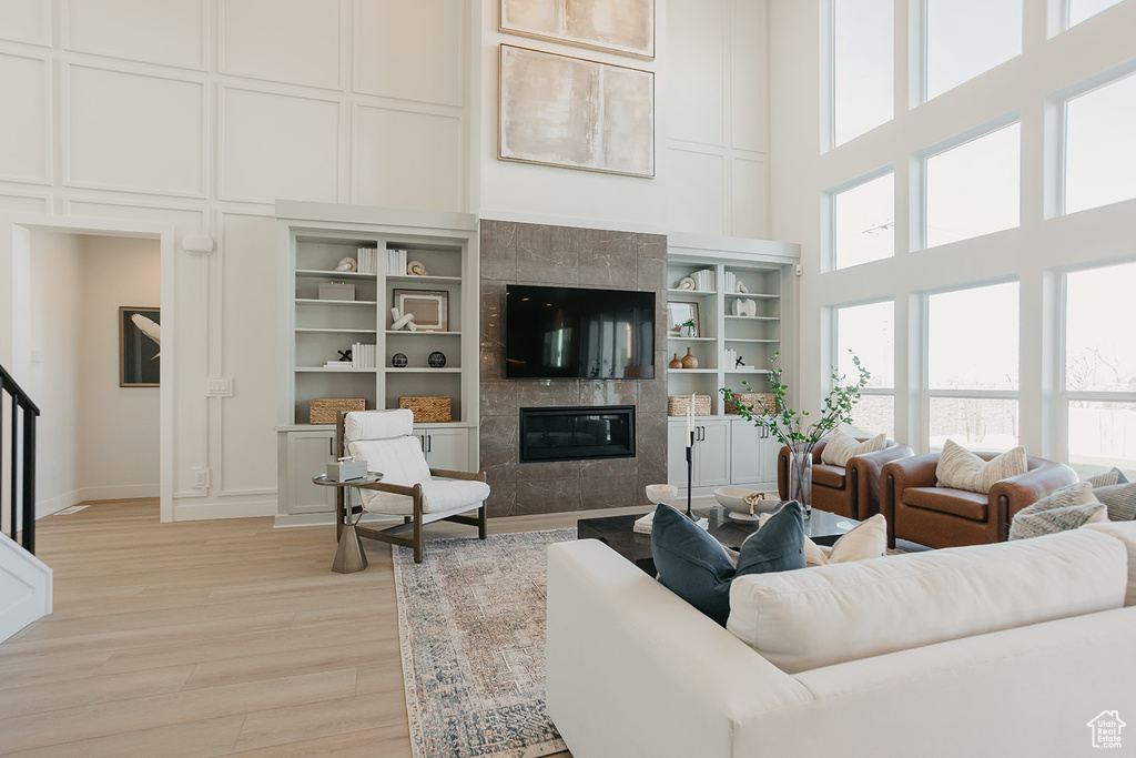 Living room with a high ceiling, a decorative wall, light wood-type flooring, and a fireplace