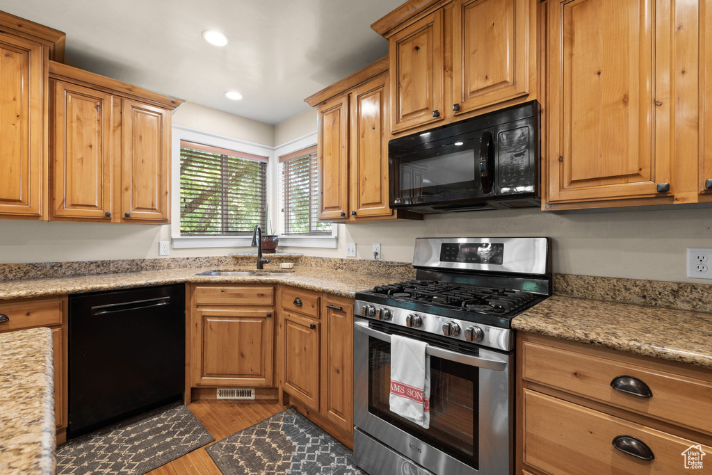 Kitchen with black appliances, wood finished floors, recessed lighting, brown cabinetry, and light stone countertops