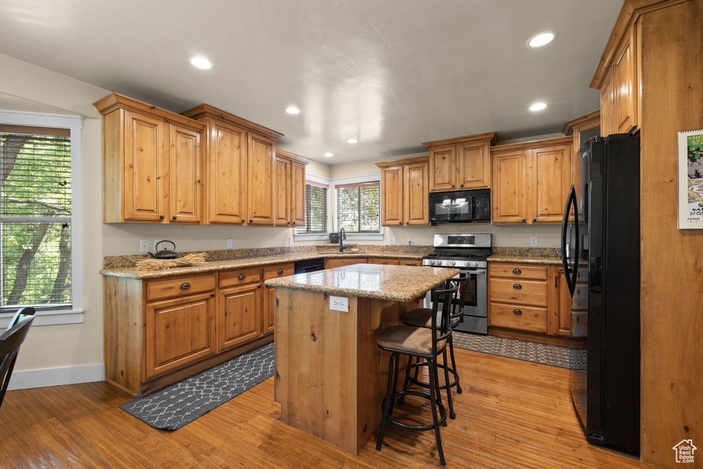 Kitchen featuring black appliances, light wood-style flooring, recessed lighting, a center island, and light stone counters