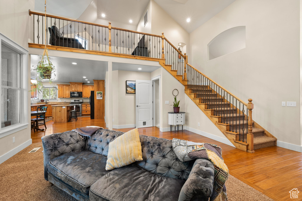 Living area featuring stairs, a towering ceiling, light wood-style flooring, and recessed lighting