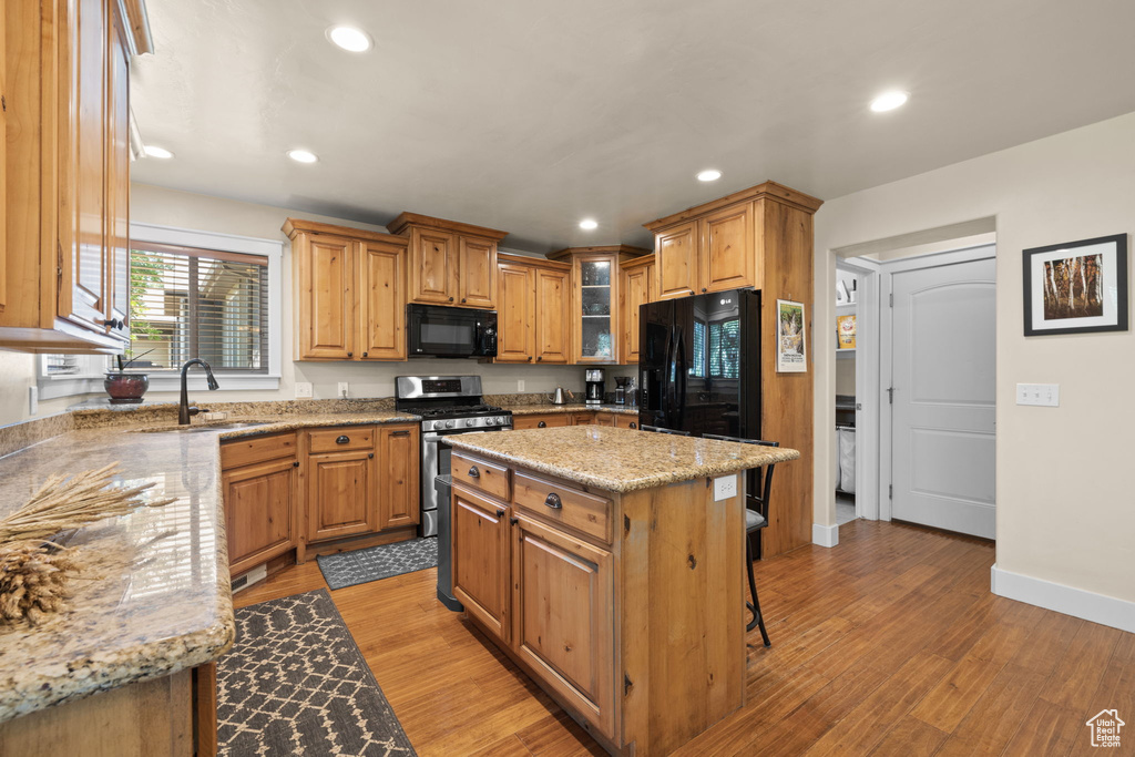 Kitchen with black appliances, light stone countertops, a kitchen bar, recessed lighting, and light wood-style flooring