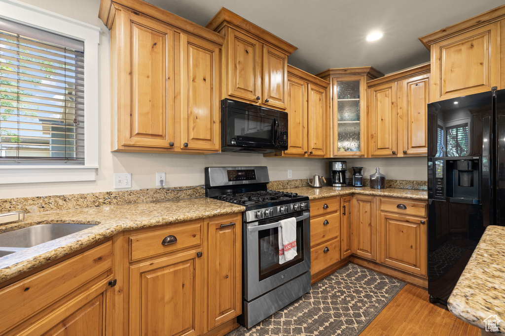 Kitchen with black appliances, dark wood-type flooring, glass insert cabinets, light stone countertops, and recessed lighting