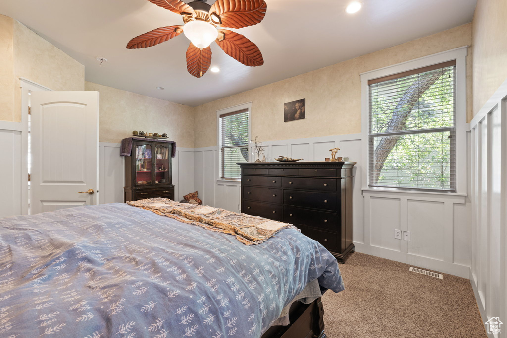 Bedroom with a decorative wall, wainscoting, carpet floors, and a ceiling fan